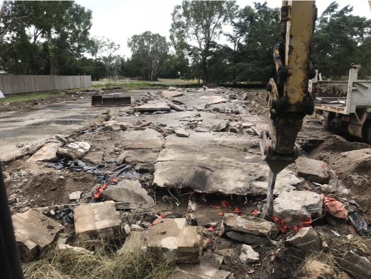 Concrete slab being broken up with a hydraulic hammer, tipper truck standing by