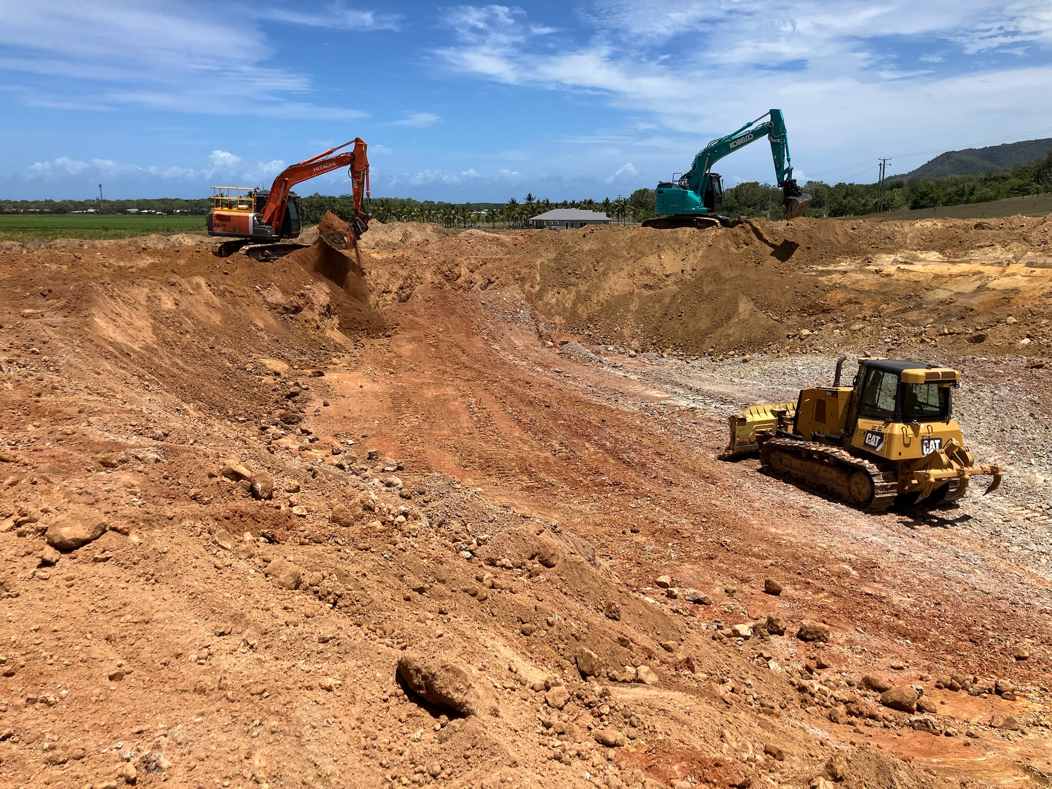 Two tracked excavators and a dozer working a bulk earthworks cut, cane and the ranges behind