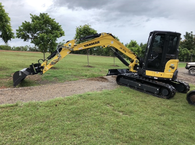 A Yanmar mini excavator parked on grass under a wet season sky